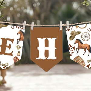 Op de afbeelding: Een banner met een western thema, met de letters "EH" en decoratieve vlaggetjes. De vlaggetjes tonen cowboyhoeden, paarden, laarzen en andere westerse motieven. De banner is opgehangen met wasknijpers aan een touw.
