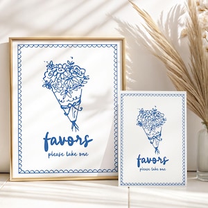 Puede incluir: Dos letreros enmarcados con una ilustración de ramo de flores azules y el texto "favors please take one". Los letreros tienen un fondo blanco con un borde festoneado azul y están en un marco dorado.