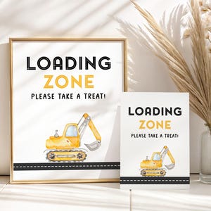 Może przedstawiać: Dwa znaki z napisem "LOADING ZONE" w kolorze czarnym i żółtym oraz "PLEASE TAKE A TREAT!" w kolorze czarnym. Jeden znak jest oprawiony. Oba znaki przedstawiają ilustrację żółtej koparki nad czarną drogą.