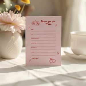 May include: A pink advice card for the bride with red text and illustrations. The card includes prompts such as "Always", "Never", and "I wish you". A white teacup and saucer are in the background.