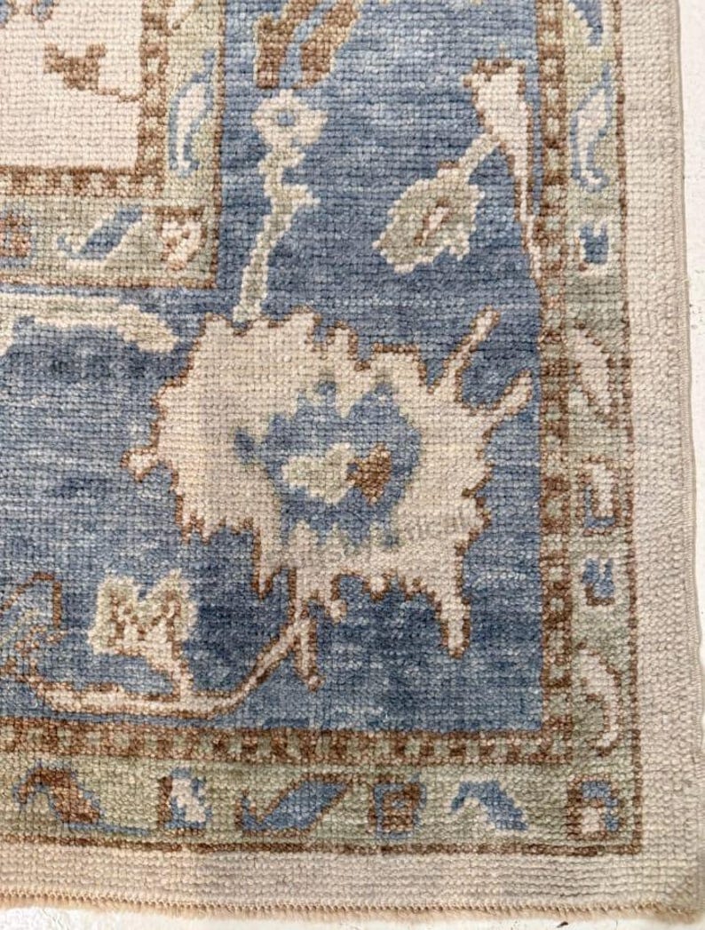 May include: Close-up of a section of a blue and beige rug with an intricate floral pattern. The rug features a central blue field with beige and brown accents, and a beige border. The design includes stylized floral motifs and geometric shapes.