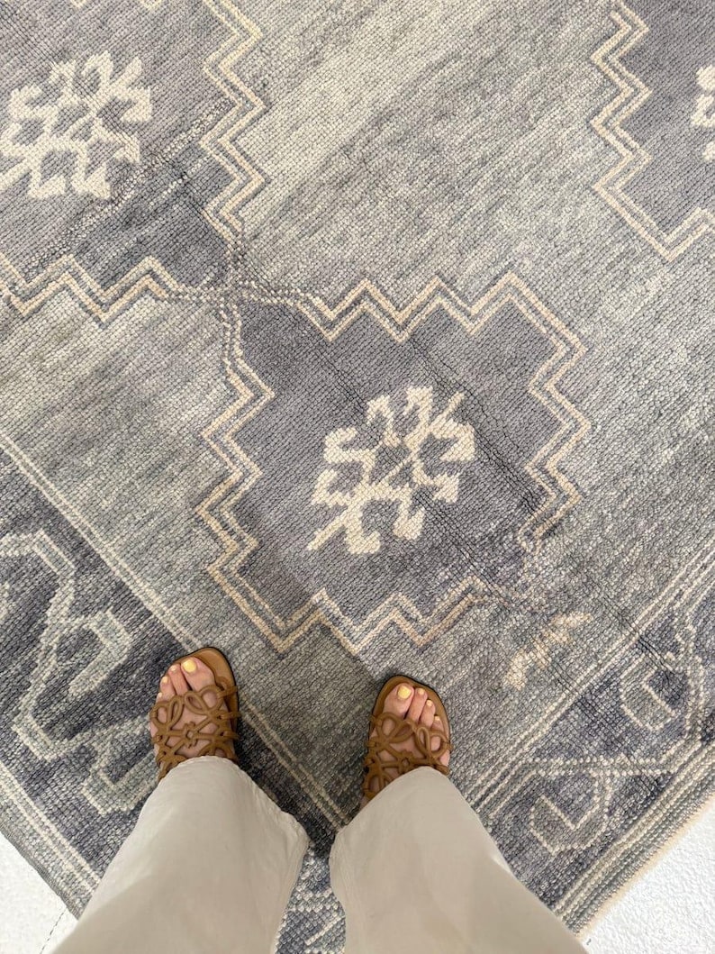 May include: A close-up view of a blue and beige patterned rug. The rug features a geometric design with a central medallion and a border. The rug's color palette includes shades of blue, beige, and white. The rug is made of a soft, textured material.