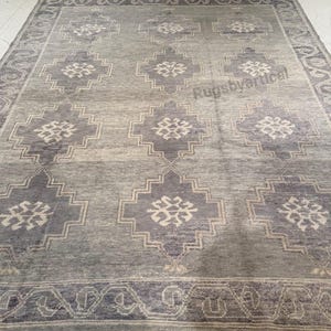 May include: A rectangular area rug in shades of gray and blue. The rug features a repeating geometric pattern of diamond shapes with floral accents. A border with a repeating design frames the rug.