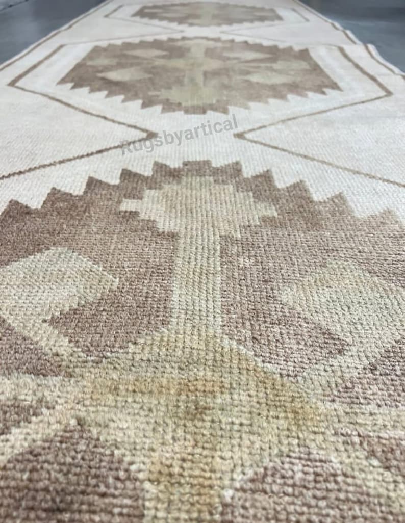 May include: A beige and brown patterned runner rug. The rug features geometric designs in shades of brown and beige. The rug's texture is visible, suggesting a woven construction. The rug is rectangular and appears to be made of natural fibres.
