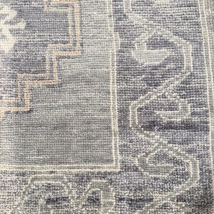 May include: Close-up of a textured, rectangular rug with a geometric pattern. The rug features a combination of light and dark blue hues, with beige and white accents. The design includes a border and central motifs.
