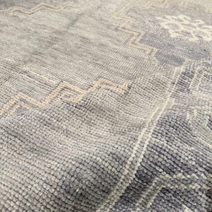 May include: Close-up of a textured, light blue rug with geometric and floral patterns in off-white and beige. The rug's surface has a soft, plush appearance, with visible woven details. The design features a repeating pattern.