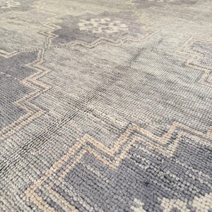May include: A close-up view of a large, patterned rug. The rug features a distressed design with a combination of light gray, dark gray, and beige colors. The pattern includes geometric shapes and a zig-zag border.