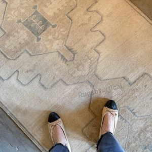 Puede incluir: Una alfombra beige y azul estampada con un diseño geométrico. La alfombra tiene un aspecto desgastado y se combina con bailarinas beige con punteras negras. El texto "Rug by artical" es visible en la alfombra.