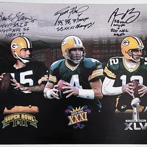 May include: A framed print depicting three Green Bay Packers quarterbacks in their uniforms, each holding a football. The print includes signatures and text indicating Super Bowl wins and MVP awards. A stadium is visible in the background.