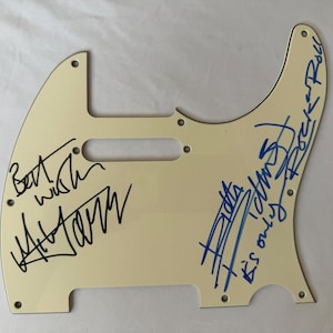 May include: Off-white guitar pickguard with signatures in black and blue ink. The signatures include the words "Best wish" and "It's only Rock n Roll". The pickguard has screw holes for mounting.