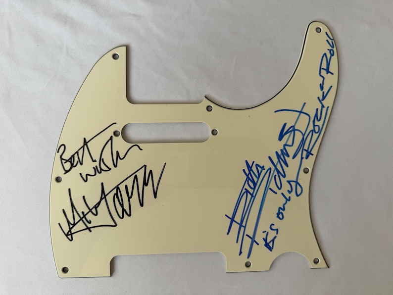 May include: Off-white guitar pickguard with signatures in black and blue ink. The signatures include the words "Best wish" and "It's only Rock n Roll". The pickguard has screw holes for mounting.