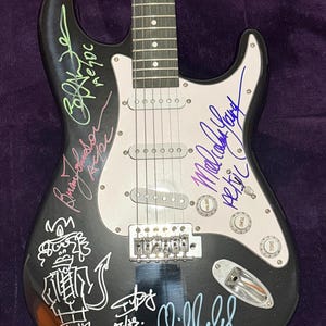Pu&ograve; includere: Chitarra elettrica nera con battipenna bianco, firmata da pi&ugrave; persone. La chitarra presenta un ponte tremolo, tre pickup e controlli di volume e tono. Sul corpo &egrave; disegnato un personaggio dei cartoni animati.