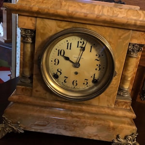 May include: Antique Seth Thomas mantle clock with a marble base and gold-tone accents. The clock face has black Roman numerals and a gold-tone hour and minute hand.