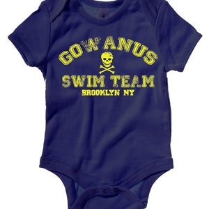 以下が含まれることがあります： 黄色のグラフィックが「GOW ANUS SWIM TEAM BROOKLYN NY」と書いてあり、ドクロとクロスボーンが描かれたネイビーブルーのベビーロンパースです。