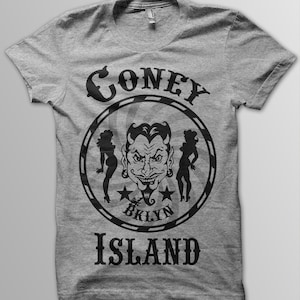 Könnte beinhalten: Graues T-Shirt mit einem schwarz-weißen Grafikdesign, das einen Teufelskopf mit zwei Frauen auf jeder Seite zeigt. Die Grafik sagt "Coney Island" mit "Bklyn" in der Mitte.