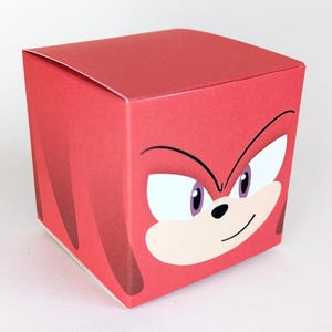 Può includere: Una scatola di cartone rossa con un viso di cartone animato di un riccio rosso con occhi bianchi e naso nero. Il riccio sta sorridendo.