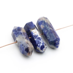 May include: Three blue and white gemstone beads strung on a copper wire. The beads are faceted and have a pointed shape.