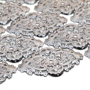 May include: A collection of silver metal decorative embellishments with a floral design. The embellishments are intricate and detailed, with a delicate filigree pattern.