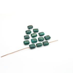 May include: A collection of twelve square-shaped green beads with natural dark green swirling patterns. Three of the beads are threaded onto a thin, straight copper-colored wire, while the remaining nine are arranged in a triangular formation.
