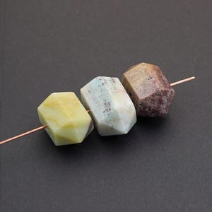 May include: Three faceted gemstone beads in yellow, blue-green, and reddish-brown are strung on a copper wire. The beads have a geometric shape and a polished surface, showcasing natural color variations. Ideal for jewelry making.