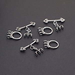 May include: Silver-toned toggle clasps, featuring a bar with decorative ends and a ring with a claw-like design. The clasps are scattered on a dark gray surface, suitable for jewelry making or crafts.