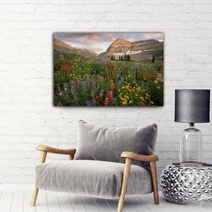 a large, colorful painting of a mountain landscape hanging on a white brick wall above a gray armchair in a living room setting.