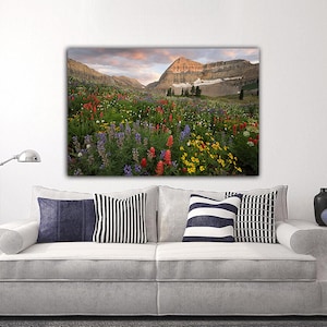 a large, colorful painting of a mountain landscape with a field of flowers in the foreground.