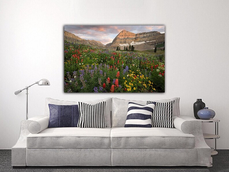 a large, colorful painting of a mountain landscape with a field of flowers in the foreground.