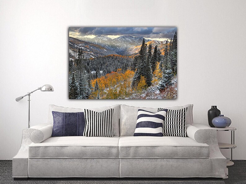 a large landscape painting hanging on a wall above a white sofa with striped pillows.