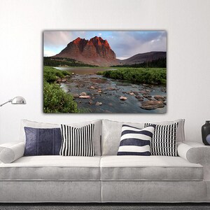 a large landscape painting hanging on a white wall above a white sofa with striped pillows.