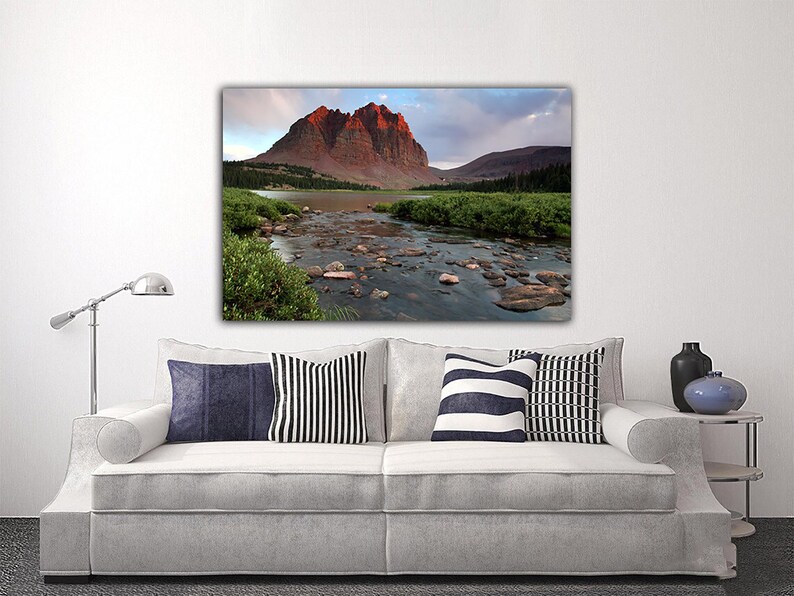 a large landscape painting hanging on a white wall above a white sofa with striped pillows.