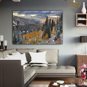 a large landscape painting hanging on a wall in a living room, depicting a snowy mountain range with trees in autumn colors.