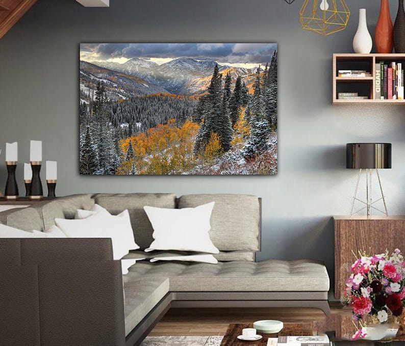 a large landscape painting hanging on a wall in a living room, depicting a snowy mountain range with trees in autumn colors.
