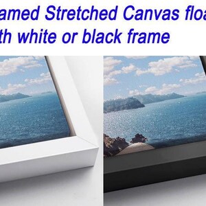 two framed stretched canvas prints, one with a white frame and the other with a black frame, both featuring a scenic landscape of a body of water and mountains.