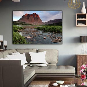 a large, framed landscape photograph of a mountain range with a river flowing through it, hanging on the wall of a modern living room.