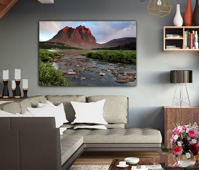 a large, framed landscape photograph of a mountain range with a river flowing through it, hanging on the wall of a modern living room.