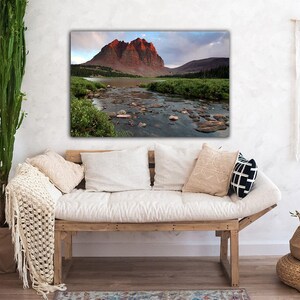 a cozy living room with a large framed landscape photograph hanging on the wall, depicting a mountain river flowing through a lush green valley.