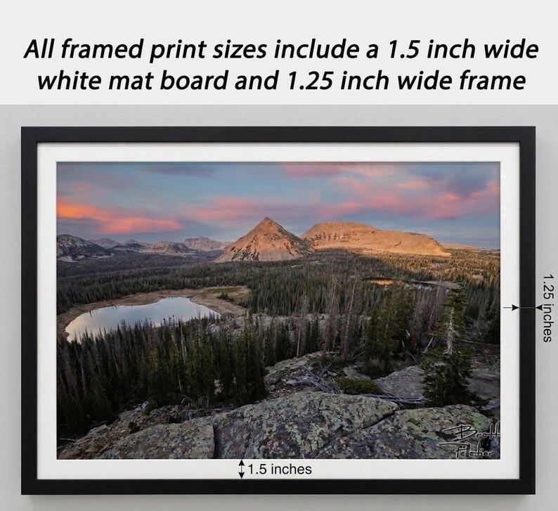 The image is a framed print depicting a scenic mountain landscape with a lake and pine trees.