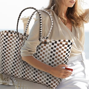 May include: A large checkered tote bag with brown, white, and black squares. The bag has two thick woven handles.