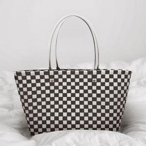 May include: A white and black checkered tote bag with white handles. The bag is made of a woven material and has a rectangular shape.
