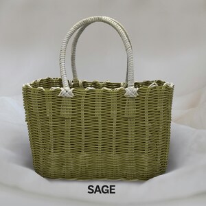 Puede incluir: Una bolsa de mano tejida de color verde salvia con asas blancas. La bolsa tiene una forma rectangular con bordes redondeados. La palabra "SAGE" est&aacute; impresa en negro debajo de la bolsa.