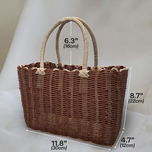 Puede incluir: Una bolsa de mano tejida de color marr&oacute;n y beige con dos asas. La bolsa mide 30 cm de ancho, 22 cm de alto y 12 cm de profundidad.