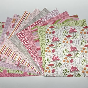 May include: A collection of square paper sheets arranged in a fan shape, featuring various patterns including red and white mushrooms, green foliage, pink stripes, plaid, and abstract dots in shades of pink, green, orange, and white.