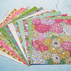 May include: A stack of patterned paper featuring floral designs in shades of pink, yellow, green, and blue. The paper is arranged in a fan shape, with the top sheet showing a large floral pattern.