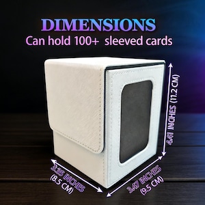 May include: A white card storage box with a flip-top lid and a window. The box is 3.35 inches (8.5 cm) wide, 3.47 inches (9.5 cm) deep, and 4.41 inches (11.2 cm) tall. It can hold over 100 sleeved cards. The word "DIMENSIONS" is at the top.