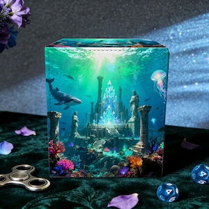 May include: A square box featuring an underwater fantasy scene with a whale, jellyfish, and a glowing crystal city. The box is on a green velvet surface, with dice and a fidget spinner nearby. The scene is vibrant with blues, greens, and coral.