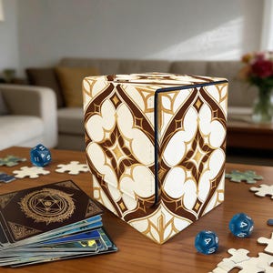 May include: A cube-shaped game box with a cream and brown geometric pattern. The box is open, revealing a dark blue interior. Dice, cards, and puzzle pieces are scattered on a wooden table. The box is approximately 6 inches wide.