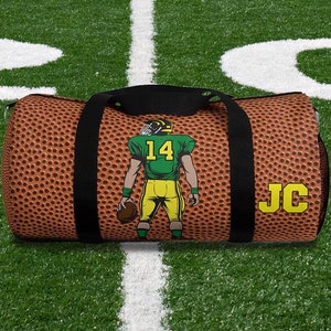 May include: A brown and black duffel bag with a football pattern. The bag has a black strap and a white and green football player graphic with the number "14" on the back. The bag also has the initials "JC" in yellow letters.
