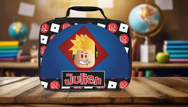 Pu&ograve; includere: Sacca da pranzo nera con un design blu e rosso che presenta un personaggio dei cartoni animati con i capelli biondi e il nome "Julian" stampato in rosso.