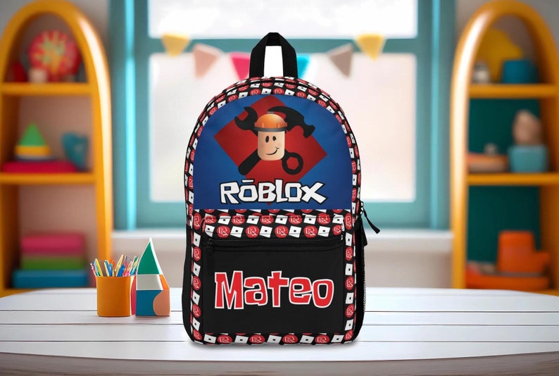 Pu&ograve; includere: Uno zaino Roblox nero e blu con un diamante rosso e un personaggio Roblox che indossa un casco. Lo zaino ha una tasca nera con il nome "Mateo" in lettere rosse.